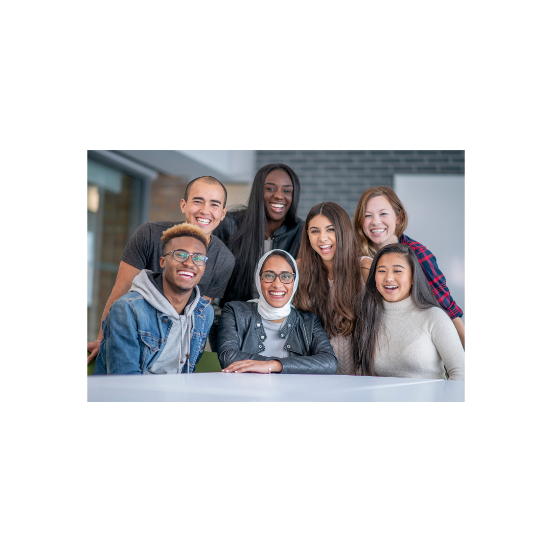 7 people gathered around a desk, all with different ethnic backgrounds, smiling at the camera.